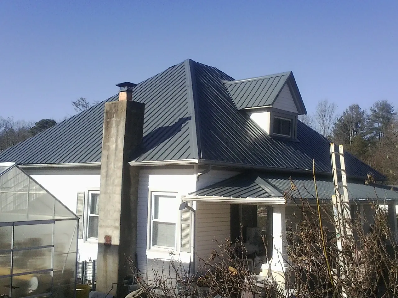 Dark blue standing seam metal roof on a white farmhouse with dormer — Slate & Tile Roof Repair by Roofing Brothers in Graceville