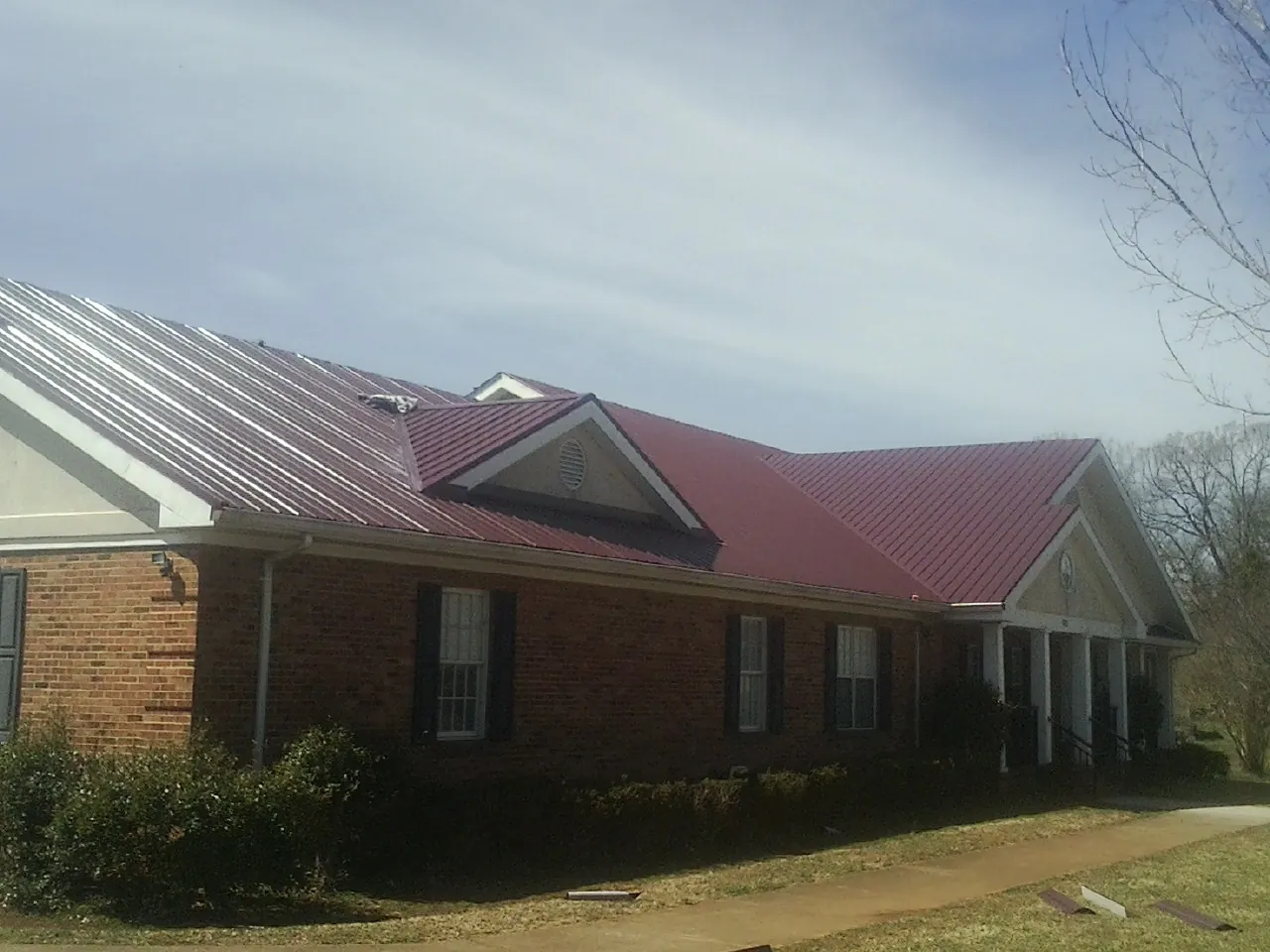 Red metal roof with gabled entries on a long brick building, from a Hail Damage Roof Repair job in Graceville