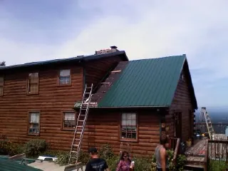 Green metal roof going on a two story log home with ladders set in Graceville
