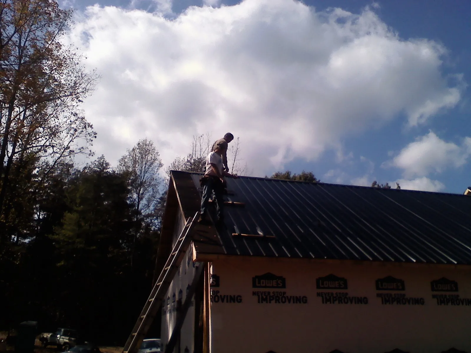 Roofer fastening dark metal panels high against a cloudy sky, from a Roof Inspection job in Graceville